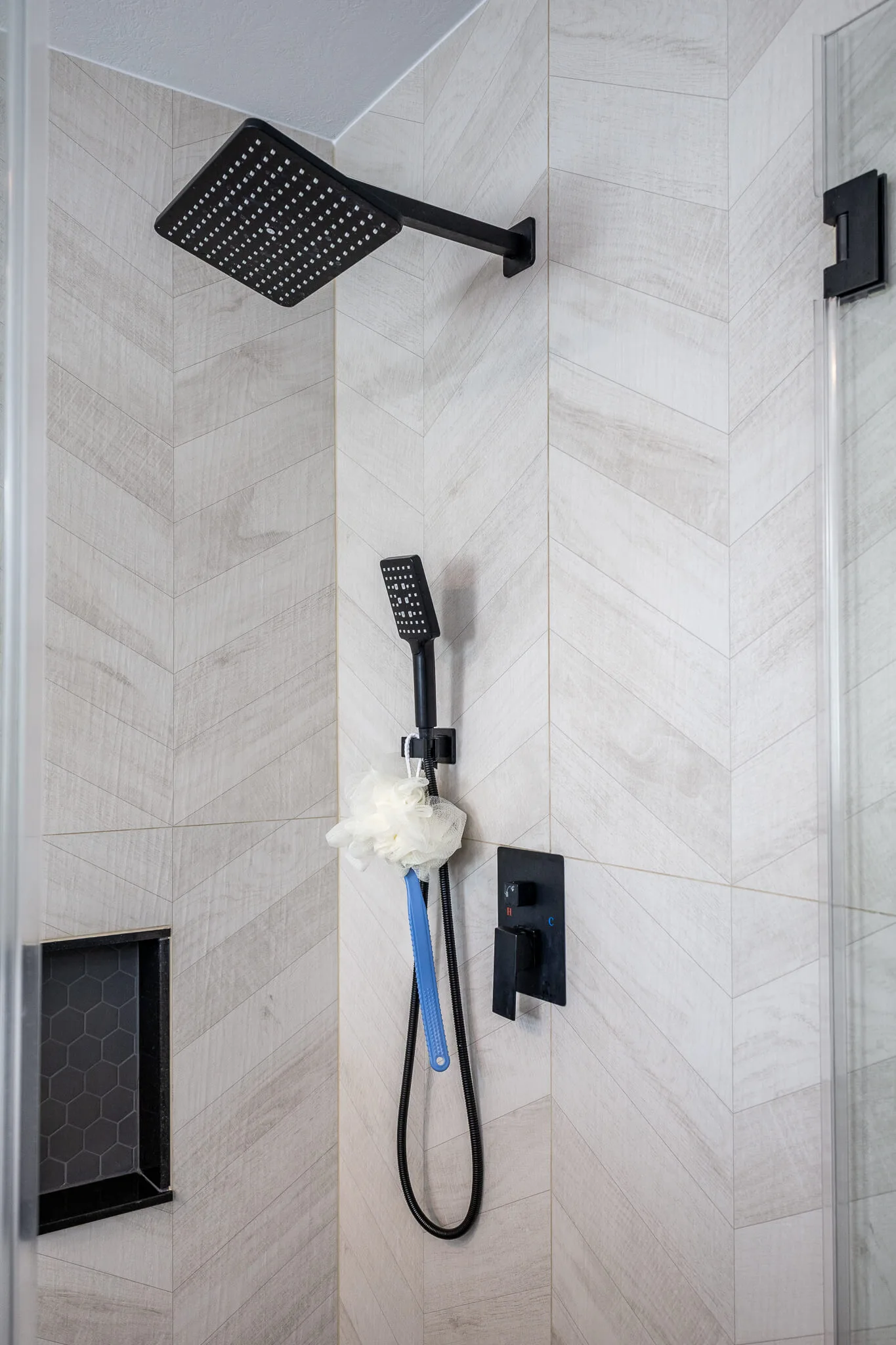 Close-up of matte black rain shower and handheld showerhead set against chevron-pattern tile walls.