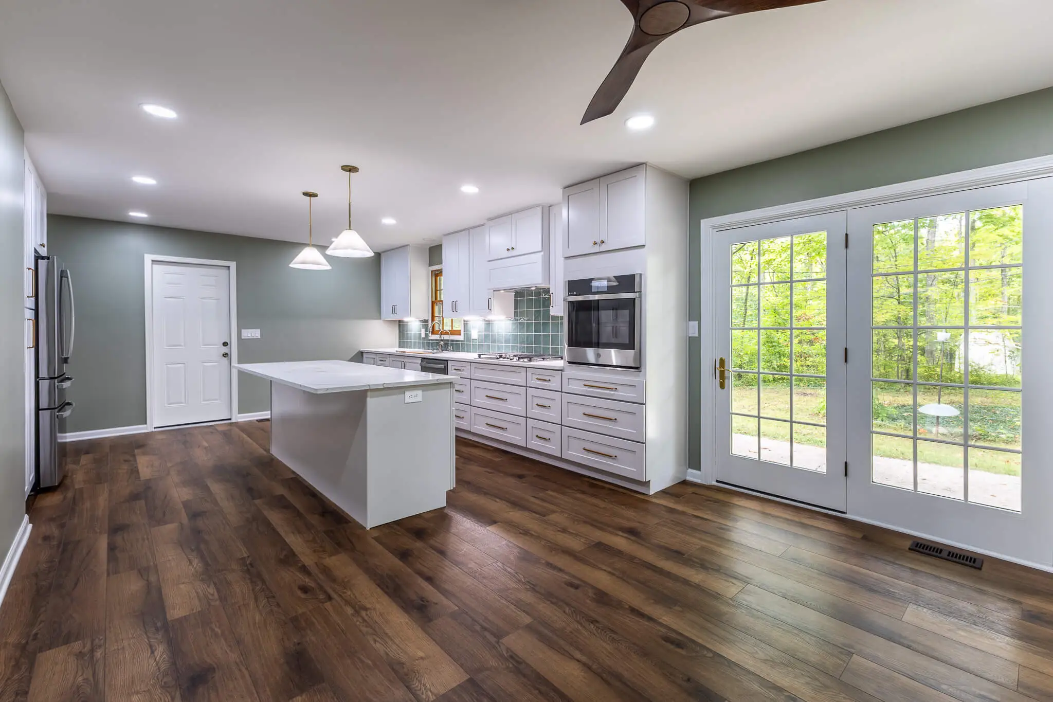 Open-concept kitchen remodel featuring hardwood floors, white cabinetry, quartz island, and French doors leading to the backyard.